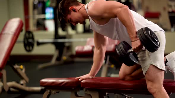 Closeup side view of young bodybuilder doing one arm dumbbell rows. alt
