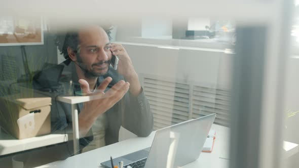 Middle Eastern Office Worker Talking on Mobile Phone and Smiling in Modern Glass Wall Office alt
