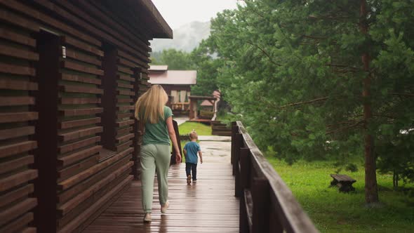Woman Chases Funny Little Boy Running Along Wooden Veranda alt