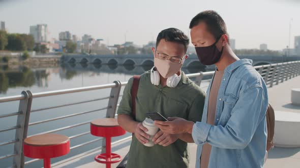 Two Asians in Face Masks Using Smartphone Outdoors alt