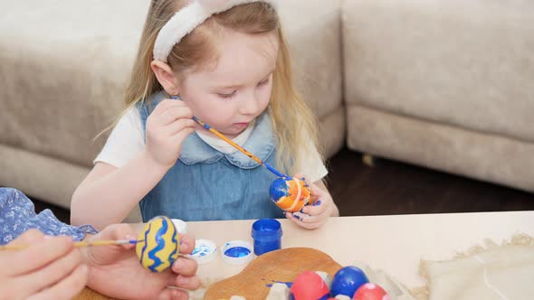 Little Girl with Rabbit Ears Decorates Easter Eggs with Paints alt