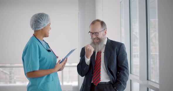 African Doctor Informing Aged Patient About Full Recovery Standing in Hospital Hallway alt