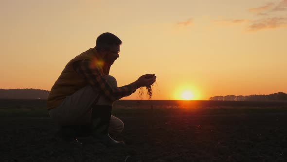 A Man Agronomist Examines the Soil in His Hands in a Field at Sunset alt