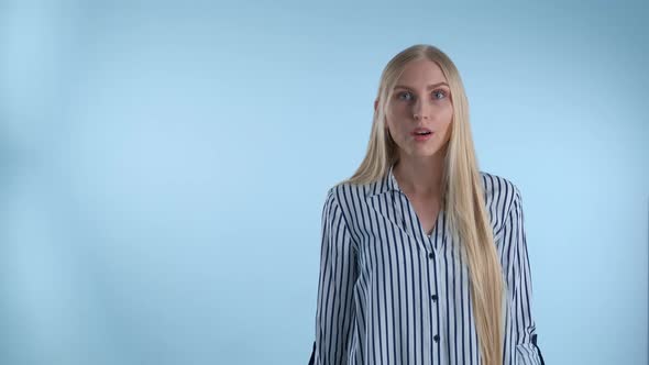 Blonde Young Woman Spreading Her Hands To the Sides and Saying "What" on Blue Background. alt