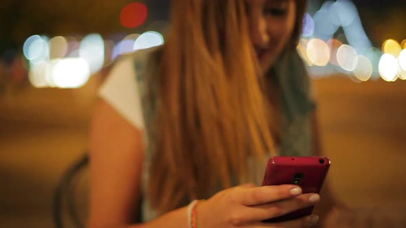 Teenage girl using smartphone to text message outdoors at night