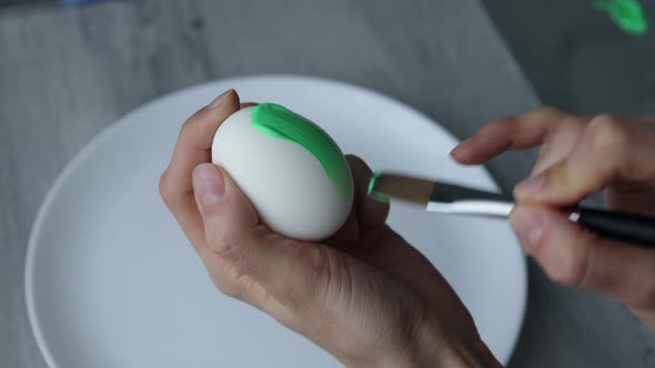 Close-up. Female hands paint Easter egg in a modern minimalist style with colorful paint.