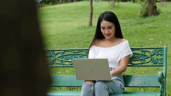 Young Asian woman using laptop at a public park.