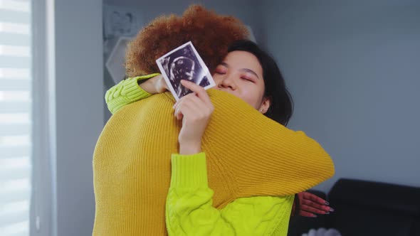 Multiracial Lesbian Couple Expecting Baby. Embracing with Ultrasound Baby Picture. Maternity Support alt