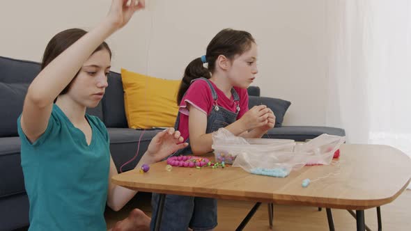 Children busy creating artwork with beads threaded on strings alt