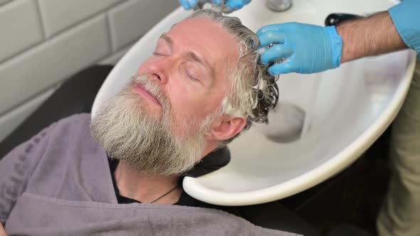Shampooing before a haircut in a barbershop. Master washes the head of a man alt