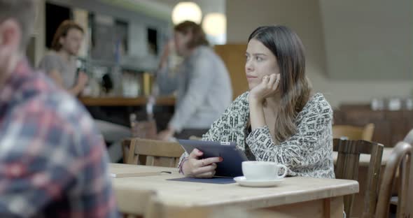 Woman thinking and using digital tablet while sitting in pub