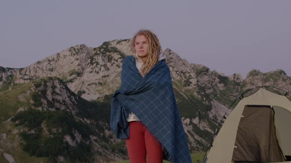 Travel Millennial woman with dreadlocks near the tent standing on top of hill looking at sunrise. alt