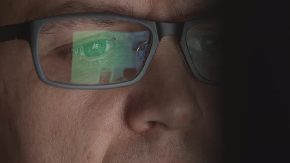 Reflection Of Scrolling Sites In An Eyeglasses Of Young Adult Man Who Works On A Computer