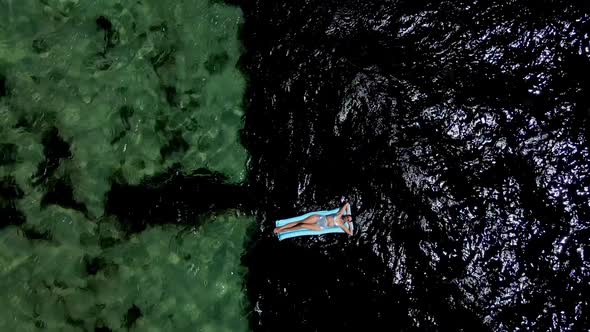 Woman Lies in a Silver Swimsuit on a Blue Inflatable Mattress in the Sea alt
