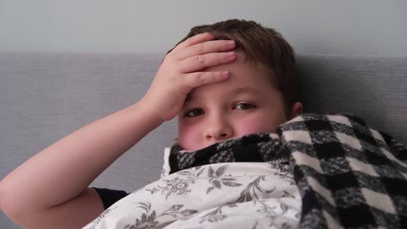 a Little Boy is Sick Lies in Bed in a Scarf Holds His Head
