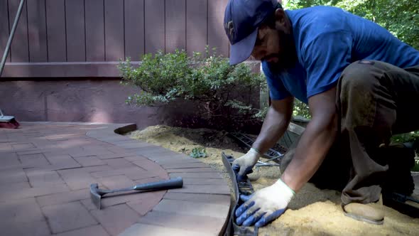 Worker takes large spike-like nails and nails the black edge retainer into place along the curving b alt