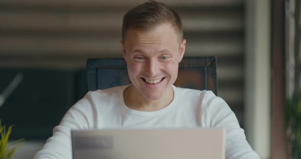 Happy Young Man Sits in Room Behind Laptop and Rejoices the Good News alt