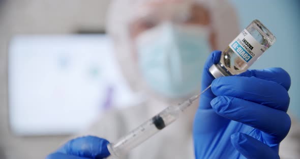 Blured Doctor's Hand Holds a Syringe and a Vaccine Bottle at the Hospital alt
