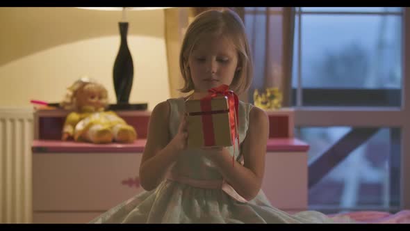 Portrait of Little Caucasian Girl Trying To Open the Casket with Red Bow alt