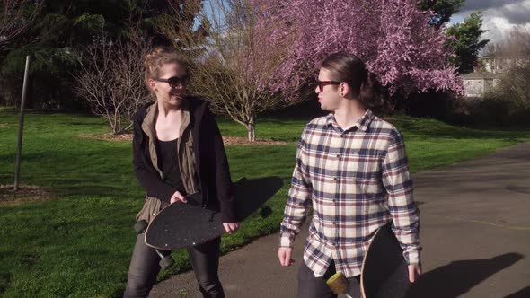 Two young people at park walking with skateboards