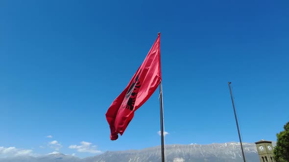 Albanian national flag flying on a flagpole, against sky.
