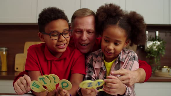 Cheerful Granddad and Smart African American Grandchildren Learning ABC Indoors alt