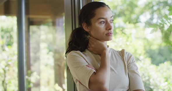 Thoughtful biracial woman standing at window and looking outside alt