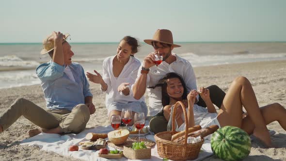 Four Happy Millennial Friends Have Picnic on Sandy Ocean Beach at Sunny Day Next Waving Sea alt