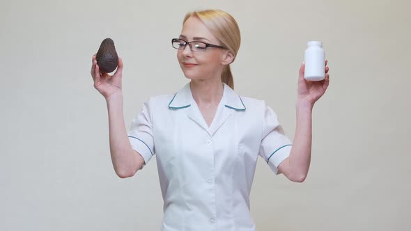 Nutritionist Doctor Holding Organic Avocado Fruit and Jar of Medicine or Vitamin or Omega 3 Capsules alt