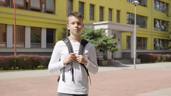 A Caucasian Teenage Boy Smiles at the Camera  a School in the Background