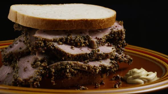 Rotating shot of delicious, premium pastrami sandwich next to a dollop of dijon mustard  alt