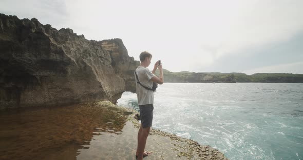 Circling Handheld View of a Male Tourist at Broken Beach Pasih Uug in Bali Taking Pictures of the alt
