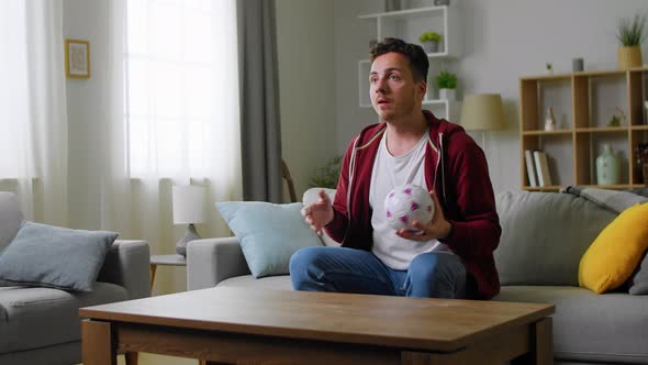 Young Caucasian Man Sitting on the Couch in the Living Room While Watching Sport Game on TV and alt