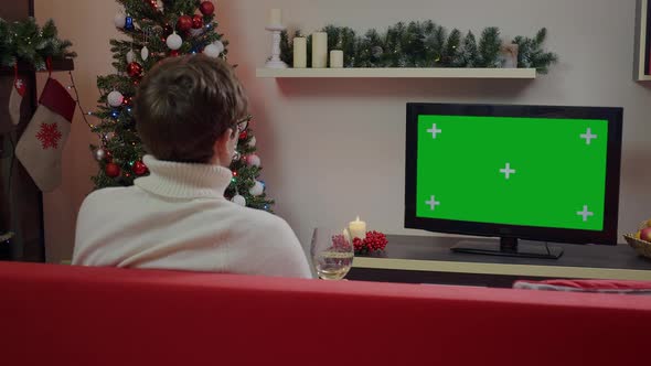 A guy wtith a glass of wine watching Green Screen Mockup TV in a Chrismas decorated living room. alt