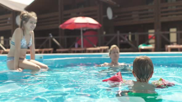Boy in Oversleeves Swims in a Pool of Clear Water with Mom and Sister on Summer Vacation alt