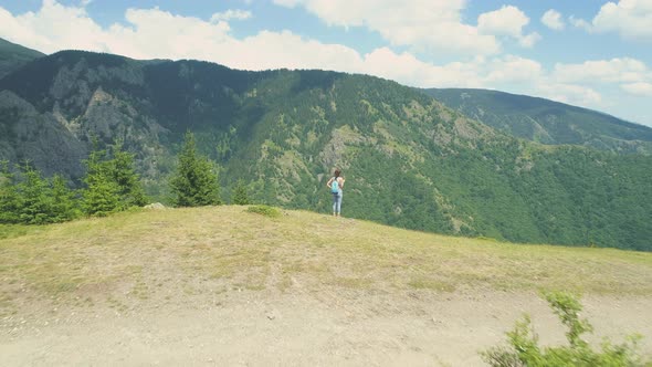 Young Woman Hiker Standing on the Mountain Edge and Looking at the Deep Valey Below alt
