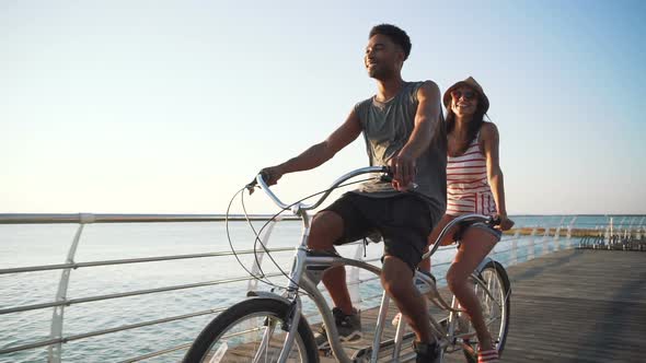 Portrait of a Mixed Race Couple Riding on Tandem Bicycle Outdoors Near the Sea Slow Motion alt