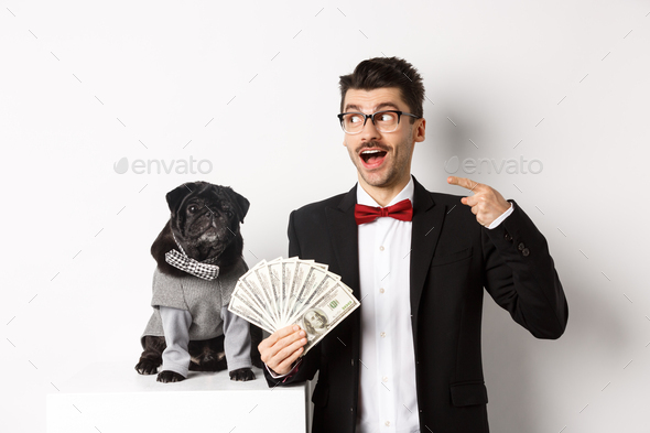Happy young man in suit earn money with his dog. Guy rejoicing, holding dollars and pointing left