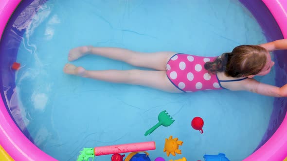 Young girl in pink swimsuit playing in colorful rainbow inflatable swimming pool on backyard