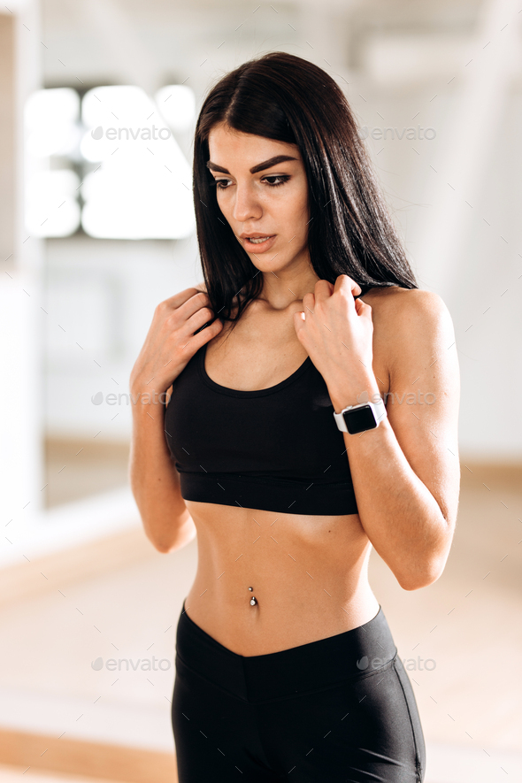 Beautiful slim girl dressed in black sportswear is standing in the gym in the fitness room next to
