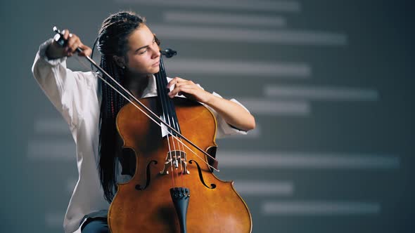 Young Beautiful Woman Playing on Cello in the Spotlight. Grey Background