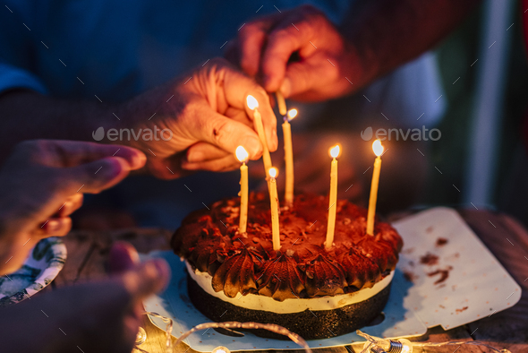 Close up of people hands fire candles on a birthday celebration cake on the table - Stock Photo - Images