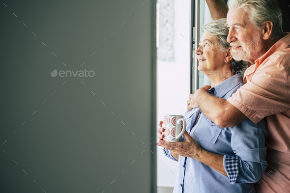 Happy senior mature couple tenderly in love at home looking outside the door window