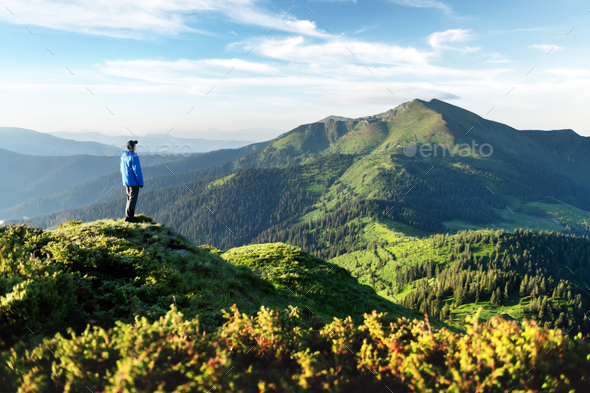 A tourist on the edge of a mountain covered with a lush grass - Stock Photo - Images