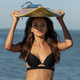 Portrait of gorgeous dark-haired girl in a black bra holds a surfboard over her head near the sea - PhotoDune Item for Sale