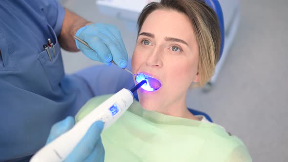 Dentist Doctor Using Dental Curing Light Equipment for Filling, Examining a Patient's Teeth in