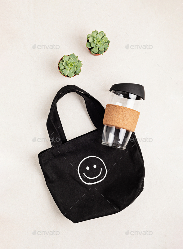 Black organic cotton cloth eco bag and reusable glass coffee cup on white background. Zero waste