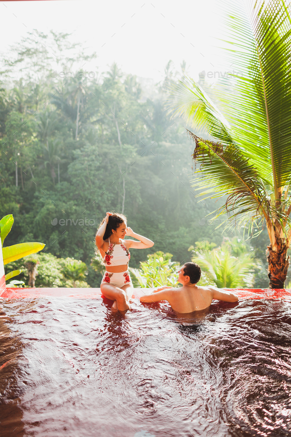 Young couple relaxing in luxury private infinity pool with amazing jungle view from above in Bali