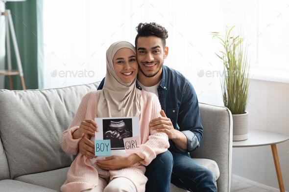 Gender Reveal. Happy pregnant muslim couple holding baby ultrasound photo at home