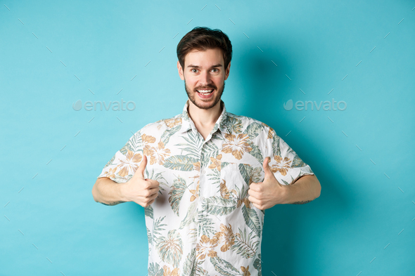 Handsome tourist showing thumbs up and say yes, praising good tourism agency, wearing hawaiian shirt
